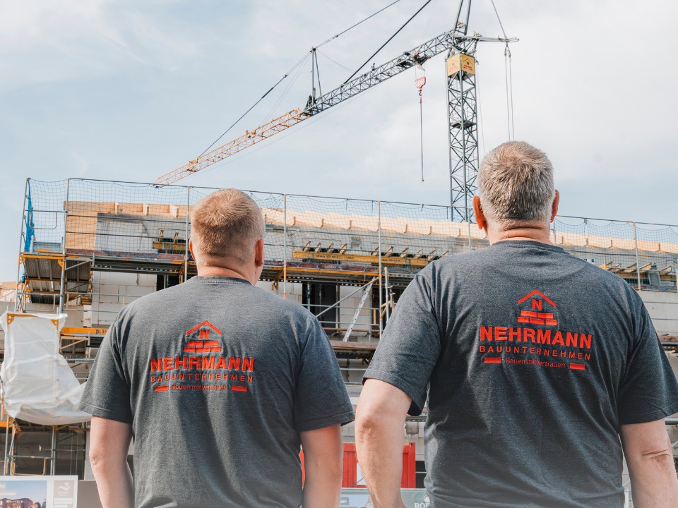 Zwei Nehrmann-Mitarbeiter blicken auf eine Baustelle mit Kran